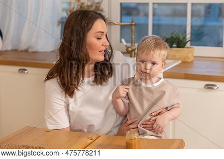Happy Family At Home. Mother Feeding Baby In Kitchen. Little Boy With Messy Funny Face Eats Healthy 