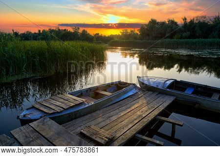 Picturesque Landscape With An Old Rustic Wooden Pier And Old Boats At Sunset Among The Reed Thickets