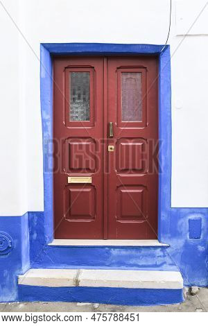 Typical Portuguese Facade With Red Wooden Door On Cobblestone Street In Evora Town, Portugal