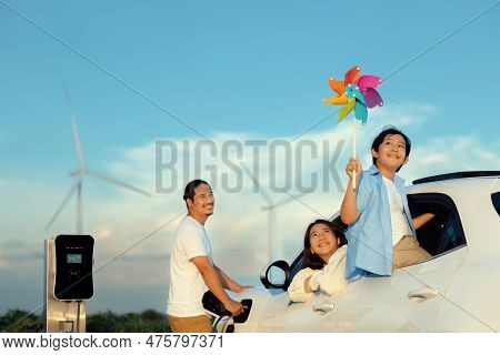 Concept Of Progressive Happy Family Enjoying Their Time At Wind Farm With Electric Vehicle. Electric