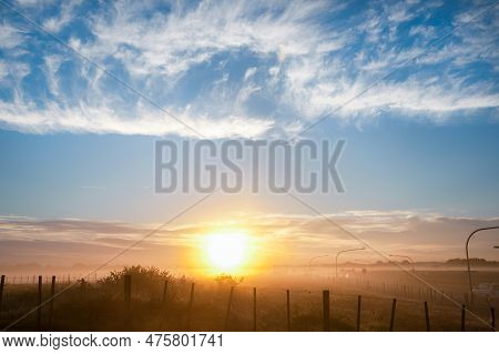 Rural Mist As Sun Illuminates Fields Under Blue Sky And White Whispy Clouds.