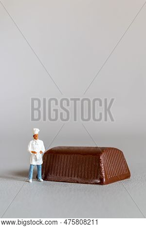 Miniature People Chef With Chocolate Standing While Standing Against A Gray Background