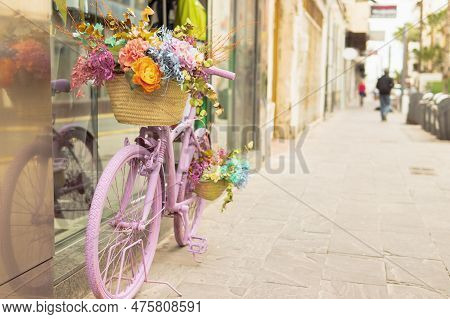 Retor Bicycle Of Pink Color Stands Near The Shop Window Decorated With Flowers
