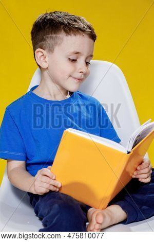 Little Cheerful Blond Green-eyed Boy 5-6 Years Old In A Stylish Blue T-shirt Holding Book And Readin