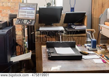 Print Center With Modern Equipment Next To Monitor And Paper Trimmer.