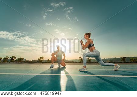 Instructor And Athlete Runner On The Track. The Athletics Marks The Time In The Lunges Exercise On A