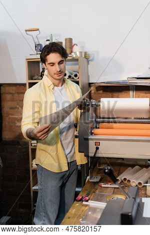 Good Looking Typographer Looking At Printed Paper Near Print Plotter.