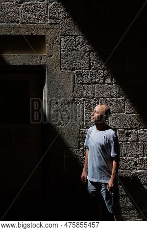 Half-bust Portrait Of A Man In A Diagonal Light Beam Crossing A Stone Wall With Windows, Contrast, L