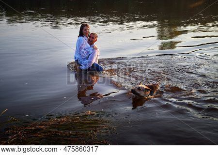 Beautiful Adult Couple Has Fun With Bug Dog Shephers In Nature In Water Of River Or Lake In Summer E