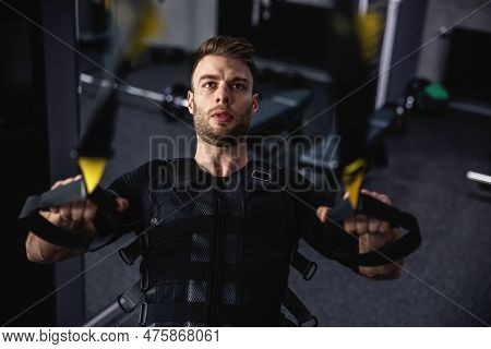A Man Exercising In The Gym On Trx Straps. A Photo Of A Young Sexy Man With Special Ems Equipment An