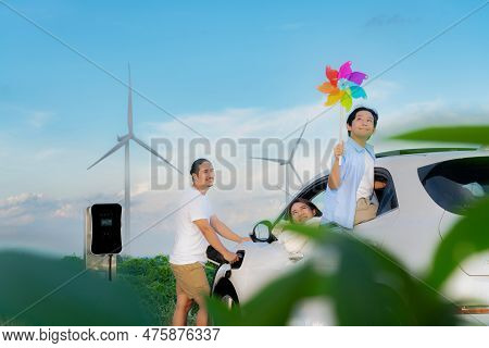 Concept Of Progressive Happy Family Holding Windmill Toy And Relax At Wind Farm With Electric Vehicl
