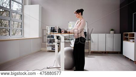 Woman Using Adjustable Height Standing Desk In Office For Good Posture