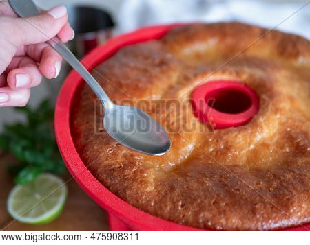 Freshly-baked Savarin In Red Silicone Cake Mold Is Poured By Syrup, Selective Focus. Rum-soaked Circ