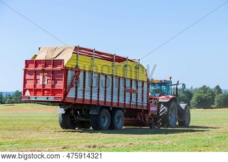 A Red Tractor With A Big Trailer Carries Silage From The Field. Agricultural Work.