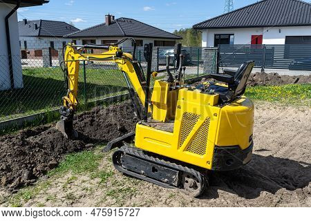 Mini Digger Digging A Hole In The Garden Along The Fence To The Drainage Pipes.