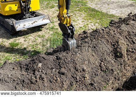 Mini Digger Digging A Hole In The Garden Along The Fence To The Drainage Pipes.