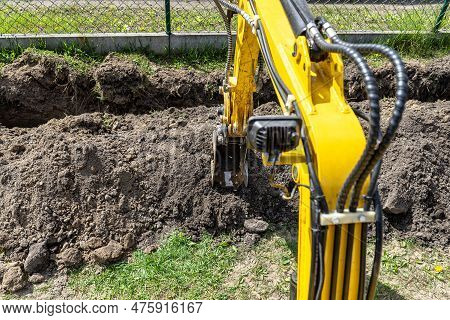 Mini Digger Digging A Hole In The Garden Along The Fence To The Drainage Pipes.