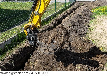 Mini Digger Digging A Hole In The Garden Along The Fence To The Drainage Pipes.