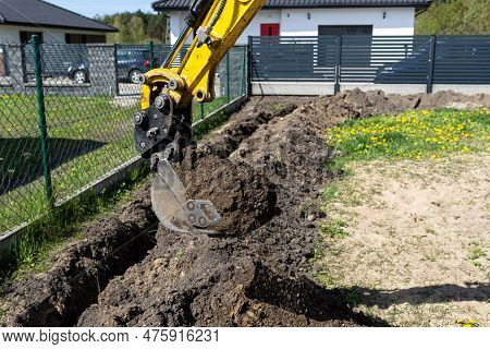 Mini Digger Digging A Hole In The Garden Along The Fence To The Drainage Pipes.