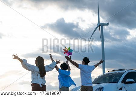 Concept Of Progressive Happy Family Enjoying Their Time At Wind Farm With Electric Vehicle. Electric