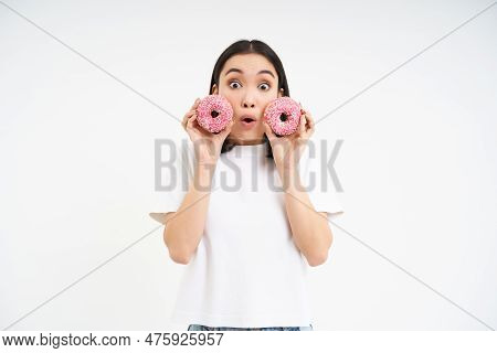 Beautiful Young Woman Eating Delicious Glazed Dougnuts, Holding Two Pink Donuts And Smiling, White B