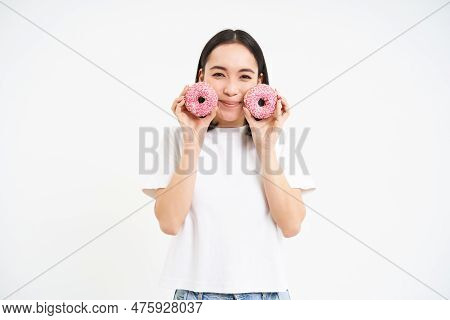 Beautiful Young Woman Eating Delicious Glazed Dougnuts, Holding Two Pink Donuts And Smiling, White B