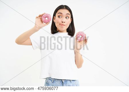 Cute Young Woman With Two Tasty Doughnuts, Tempted To Try Glazed Donnuts, White Background