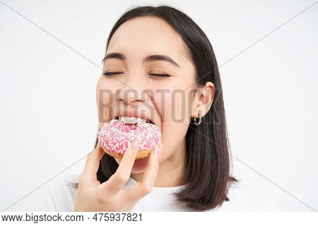 Close Up Of Smiling Pleased Asian Woman, Eats Glazed Pink Doughnut, Enjoys Eating Tasty Donnut, Whit