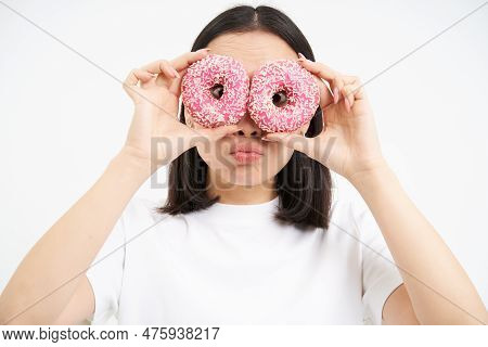 Close Up Portrait Of Funny Asian Girl Looks Through Donnut Holes, Holding Two Glazed Doughnuts And M