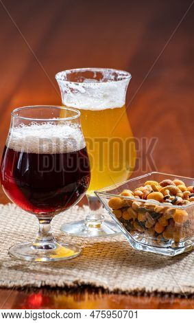 Glasses Of Belgian Yellow Blond And Dark Brown Beer Made In Abbey Served In Bar With Party Nuts, Clo