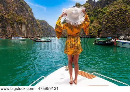 Beautiful Young Blonde Woman In Orange Dress On A Boat Staying Back With White Hat During Excursion