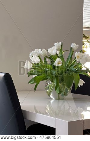 White Tulips In Glas Vase On White Table And Black Chairs, Home Interior