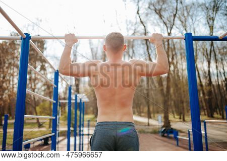 Outdoor Workout Guy Performs Intense Pull-ups On A Bar. A Fit Male Trains His Upper Body By Doing Na