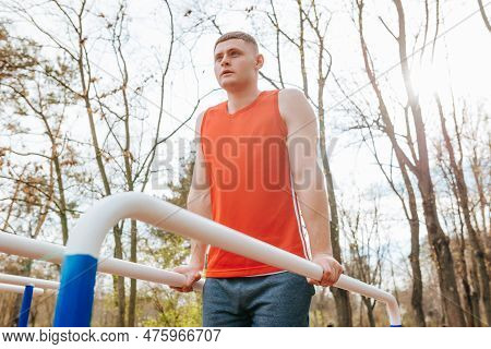 Red T-shirt, Strong Determination A Male Athletes Outdoor Workout. The Parallel Bars Provide The Per