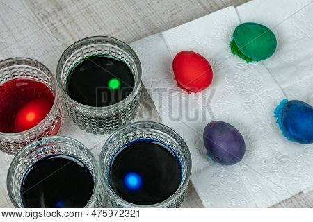 Easter Chicken Eggs Are Dyed In Glass Cups With Green Blue Purple Red Food Coloring. The Concept Of 