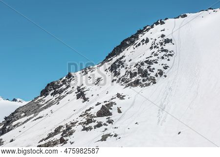 Climbers Footprints On Steep Snowy Slope Of High Snow Mountain With Rocks On Top. Snow-white Mountai