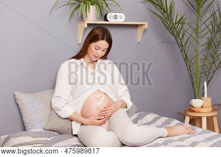 Young Pregnant Woman With Bare Belly Sitting In Bedroom, Enjoying Peaceful Moment While Awaiting Bab