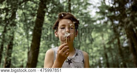 Boy In His Early Teens Blowing Dandelion Bulb To Spread The Seeds In A Beautiful Green Spring Forest
