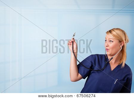 Pretty young nurse in hospital listening to empty copy space with sthetoscope