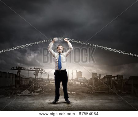 Young furious businessman breaking metal chain with hands
