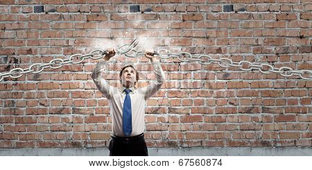 Young furious businessman breaking metal chain with hands