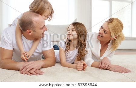 family, children and home concept - smiling family with and two little girls lying on floor at home