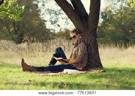 Hipster style young woman reading a book in autumn park during picknic