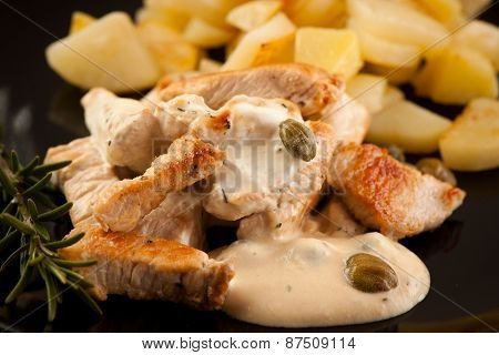 Grilled Turkey Meat With Cheese Sauce And Capers On Black Plate With Potatoe And Branch Of Rosemarry