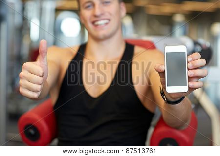 sport, bodybuilding, lifestyle, technology and people concept - happy young man with smartphone showing thumbs up in gym