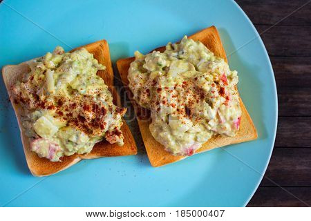 Two sandwiches with avocado salad on blue plate. Crunchy toast with vegetarian salad. Avocado and mayonnaise with egg and paprika. Healthy breakfast. Vegetarian fast-food. Whole-grain bread snack