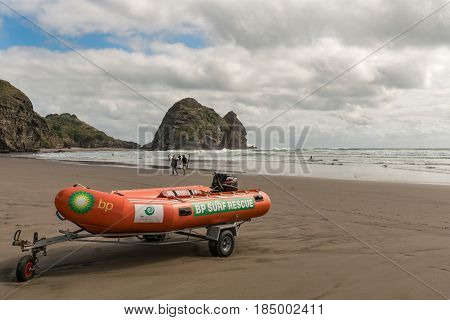 Auckland New Zealand - March 2 2017: Closeup of orange dinghy boat of beach life guard at Piha Beach with Rabbit rock in the back. Tasman sea surf and people.