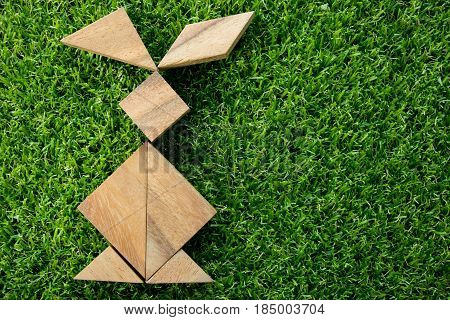 Wooden tangram puzzle in rabbit shape on artificial green grass background (Concept of Happy Easter)