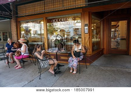 HARBOR SPRINGS, MICHIGAN / UNITED STATES - AUGUST 4, 2016: People enjoy eating Kilwin's ice cream, at tables outside of store's front window, during the Street Musique event on Main Street in downtown Harbor Springs.