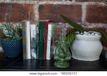 Home interior decor a ceramic statuette of Ganesh books and flower pots with plants on black wooden commode on a red brick wall background